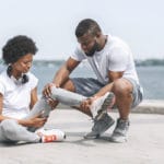 Man helps woman with injury on the sea shore | Featured image for ankle sprain symptoms.