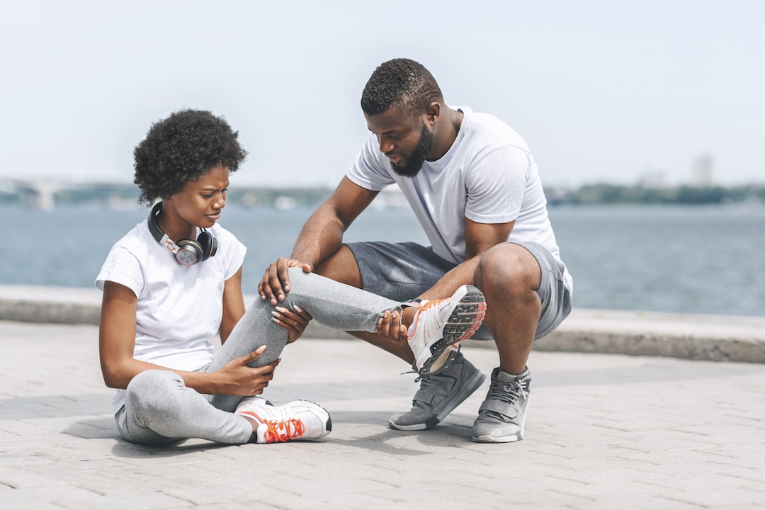 Man helps woman with injury on the sea shore | Featured image for ankle sprain symptoms.