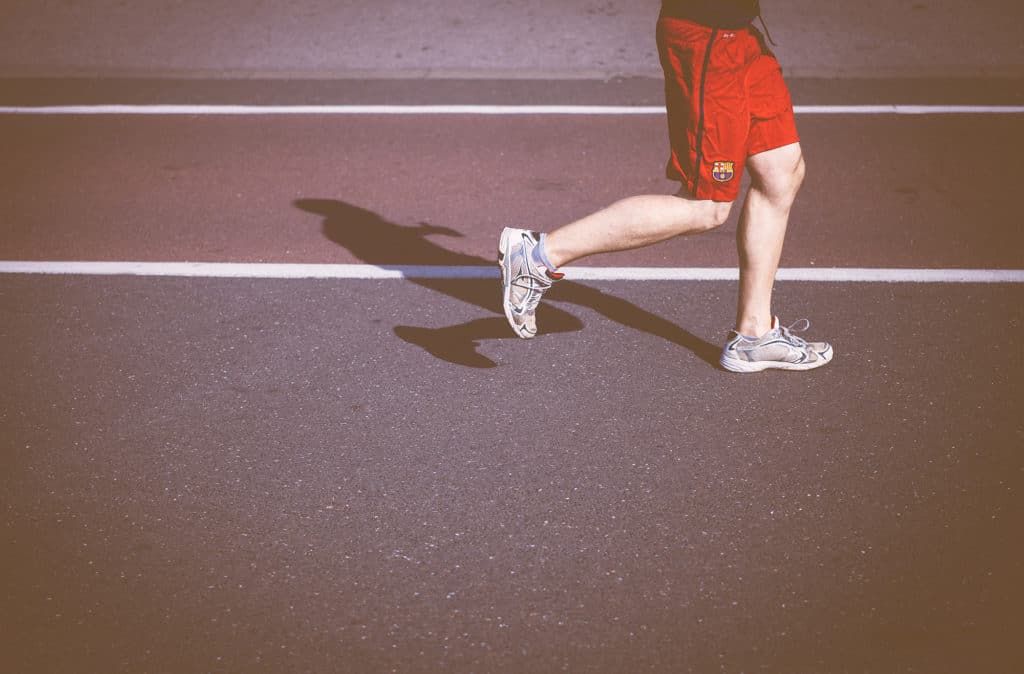 Person running on a track | Featured image for Patella Femoral Pain Syndrome Article.