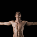 Topless person standing with arms wide open on black background.