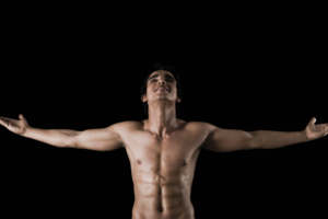 Topless person standing with arms wide open on black background.