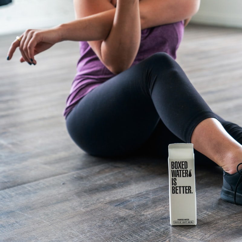 Image of women with purple tank top stretching next to Boxed water