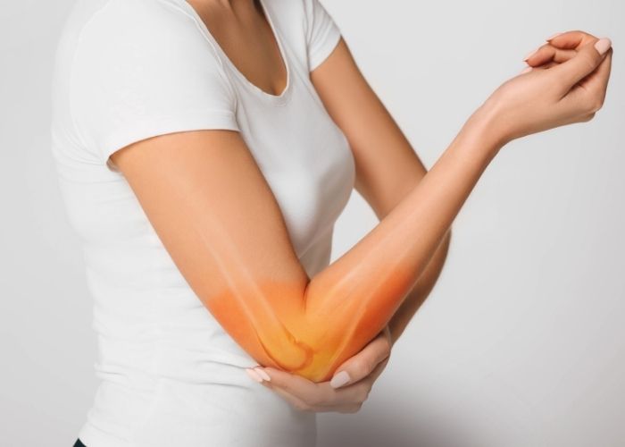 A woman's torso holding her elbow with her elbow highlighted to display pain | Featured image for Throwers Elbow.