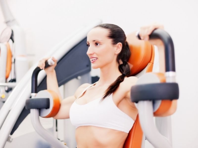 A close up of a woman's upper body while using gym equipment | Featured image on Pectoralis Major Muscle Strains.