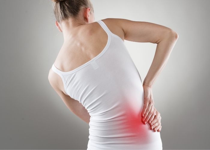 A woman's back leaning to one side and holding her right hip with a red mark on her side to show you where the pain is located | Featured image on Hip Physiotherapy.