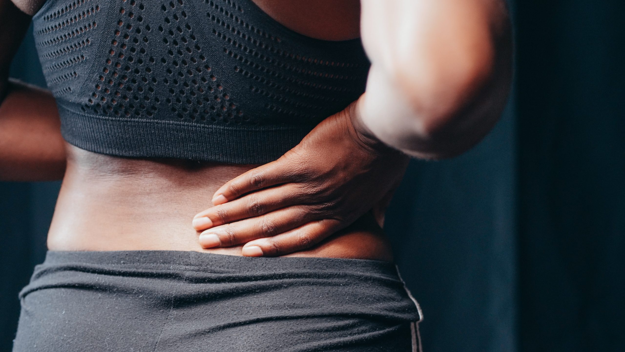 A close up of a woman with her hand pressed on her back | Featured image on Types of Pain.