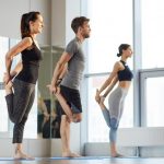 Three people standing on yoga mats holding one of their legs and stretching | Featured image on Osteitis Pubis.