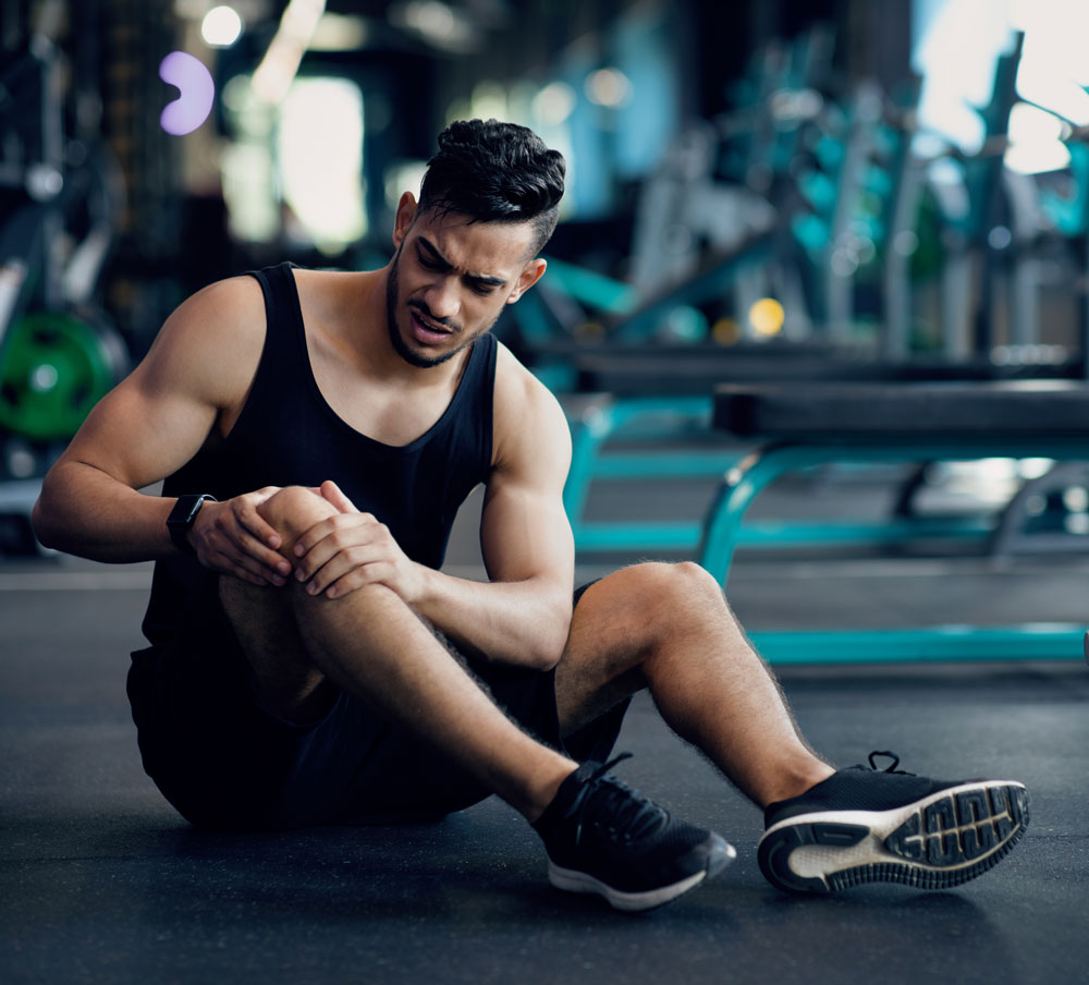 A man sitting on the floor holding his knee that is in pain | Featured image on ITB Friction Syndrome.