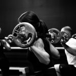 Black and white photo of a woman lifting a barbell from a squat position Featured image for Importance of Progressive Overload blog for Pivotal Motion Physiotherapy.