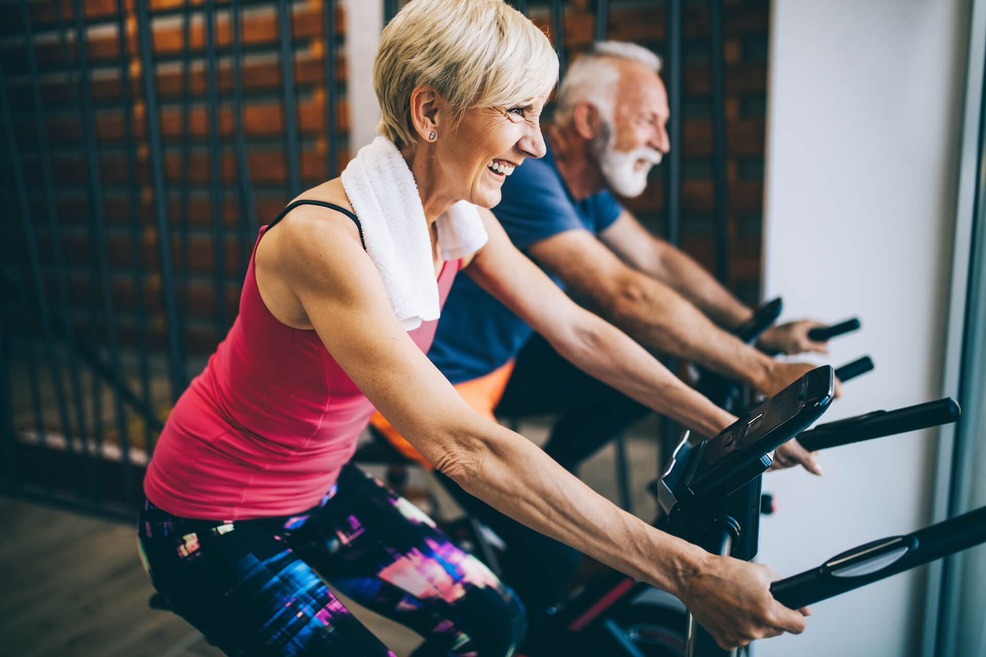 Two smiling older people exercising on bikes | Featured image for the Type 2 Diabetes Management page at Pivotal Motion Physiotherapy.