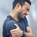 Athletic young man grabbing his shoulder in pain | Featured Image for the Calcific Tendonitis Shoulder Treatment Page of Pivotal Motion Physiotherapy.